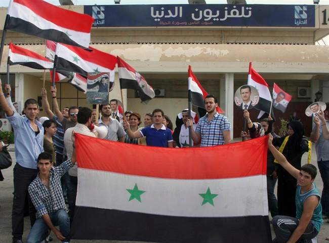 Pro-Syrian regime protesters hold Syrian flags and portraits of Syrian President Bashar Assad, on the airport highway near Damascus, Syria, Sept. 26, 2011.
