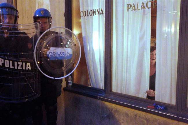 A woman is seen through a restaurant window, right, as Italian policemen in riot gear patrol in front of the Parliament, in Rome, Wednesday, Sept. 7, 2011. Italy's upper house of parliament has approved the government's disputed austerity package aimed at reducing the country's deficit by more than Ä54 billion ($70 billion) over three years. The Senate voted 165-141 with three abstentions to approve the package, which was put to a confidence vote to ensure Premier Silvio Berlusconi's allies united behind the government after weeks of bickering over details of the plan. (AP Photo/Pier Paolo Cito).