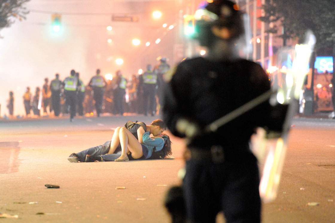 Riot police walk in the street as a couple kiss on June 15, 2011 in Vancouver, Canada. Vancouver broke out in riots after their hockey team the Vancouver Canucks lost in Game Seven of the Stanley Cup Finals.