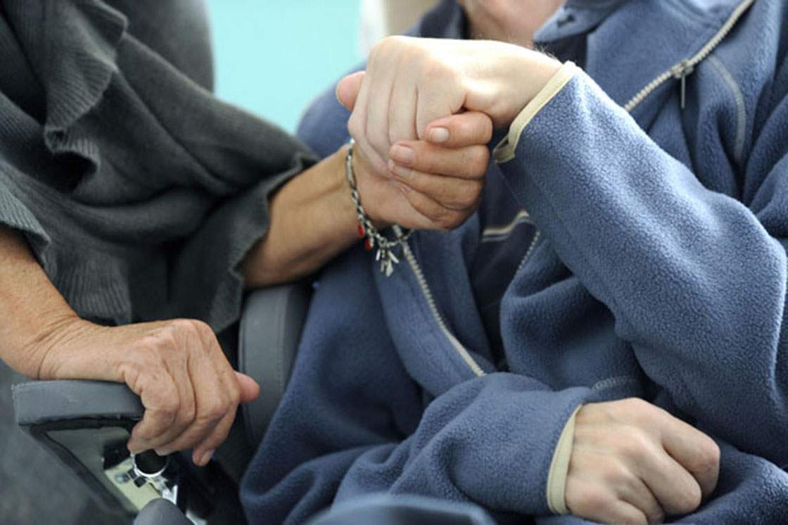 A woman (L) holds the hand of her husband who lives with Alzheimer's disease.
