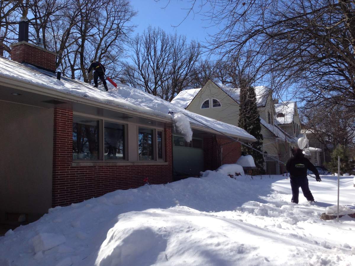 Workers shovel snow off the roof of a Kingston Row home Monday (March 25, 2013).