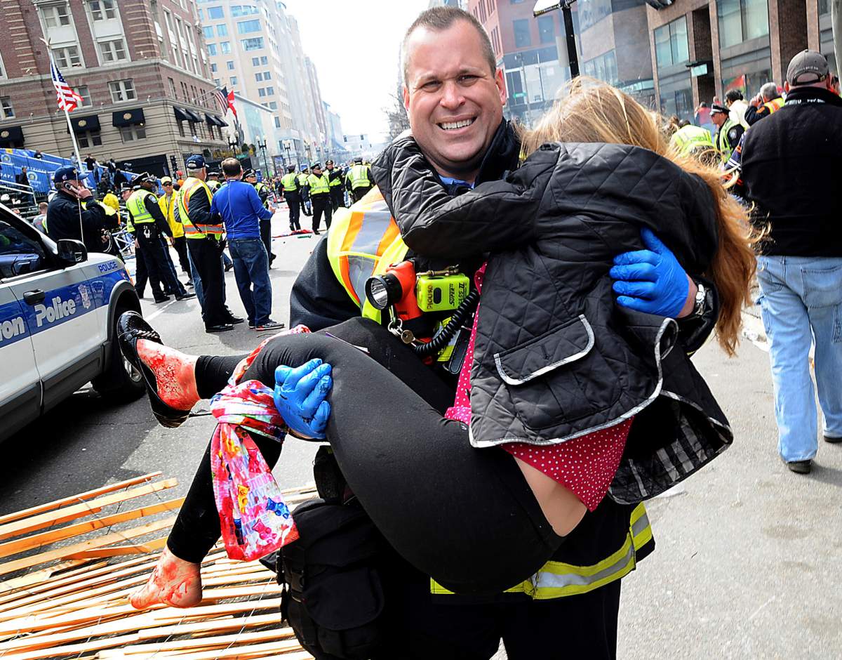 In this Monday, April 15, 2013 photo, Boston Firefighter James Plourde carries an injured girl away from the scene after a bombing near the finish line of the Boston Marathon. (AP Photo/MetroWest Daily News, Ken McGagh).