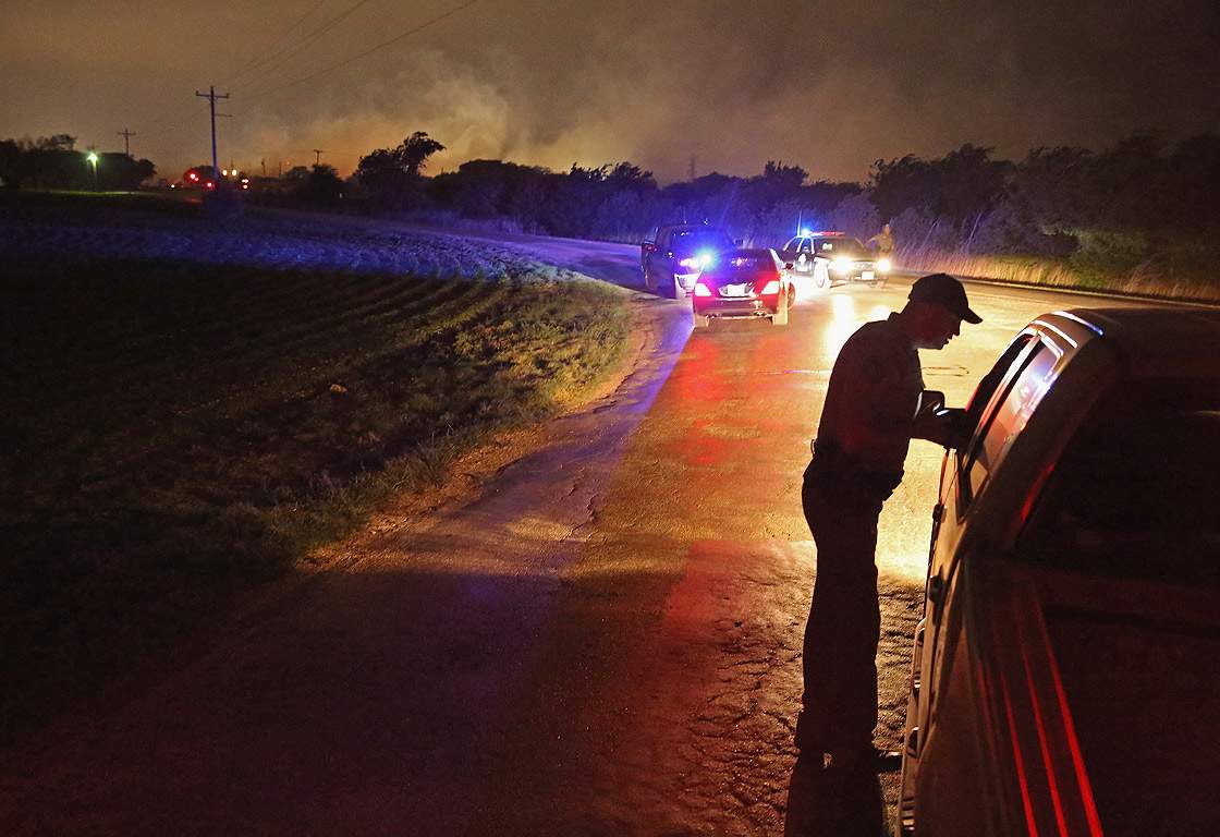 With smoke rising in the distance, a law enformcement officer runs a check point at the perimeter about half a mile from the West Fertilizer Company April 18, 2013 in West, Texas.