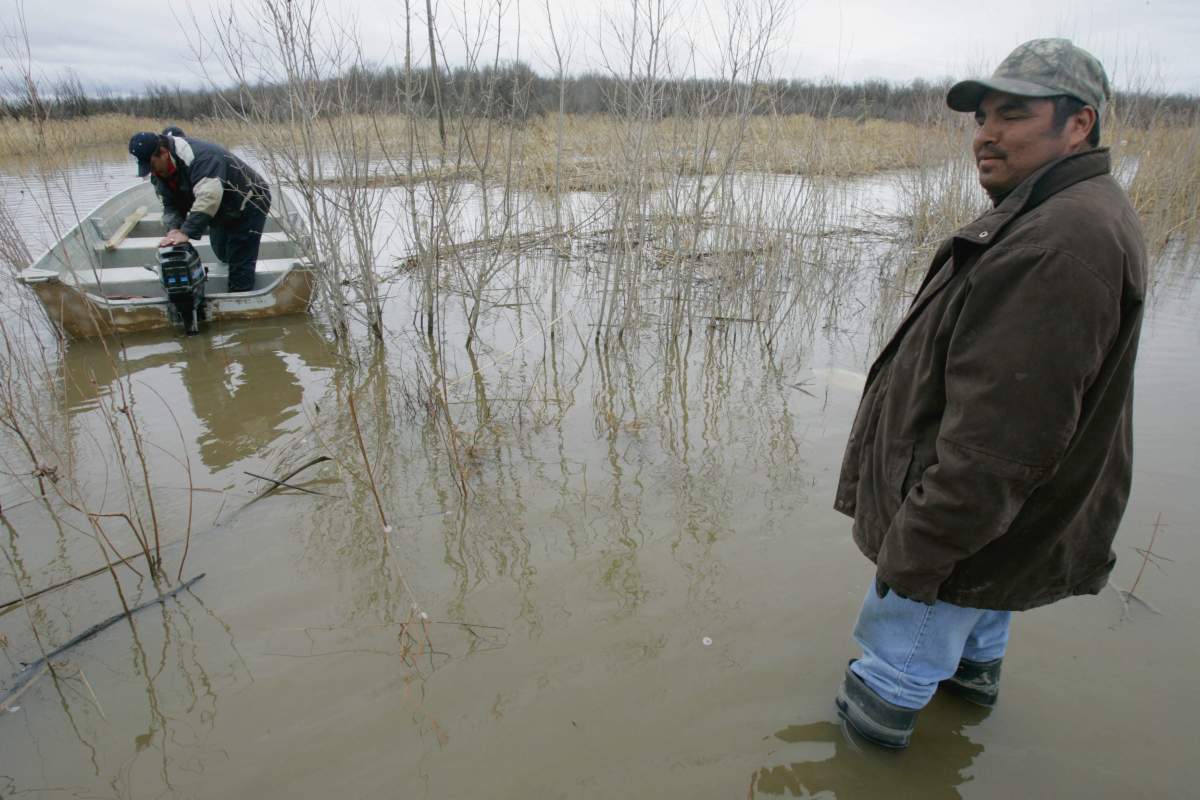 Telbert Head, right, of the Red Earth First Nation stands knee deep in flood water while Wilson McKay attempts to start a boat Monday, April 17, 2006 .