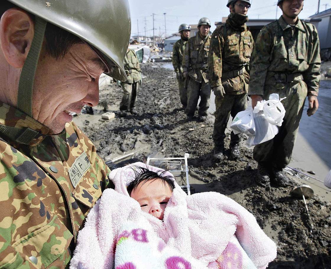 A soldier smiles as he holds a four-month-old baby who survived the recent tsunami with her family at Ishinomaki city in Miyagi prefecture on March 14, 2011.