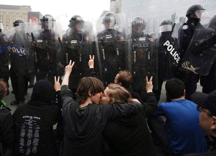 Two activists kiss while protesting in front of a line of riot police during the G20 Summit in Toronto Saturday, June 26, 2010. 