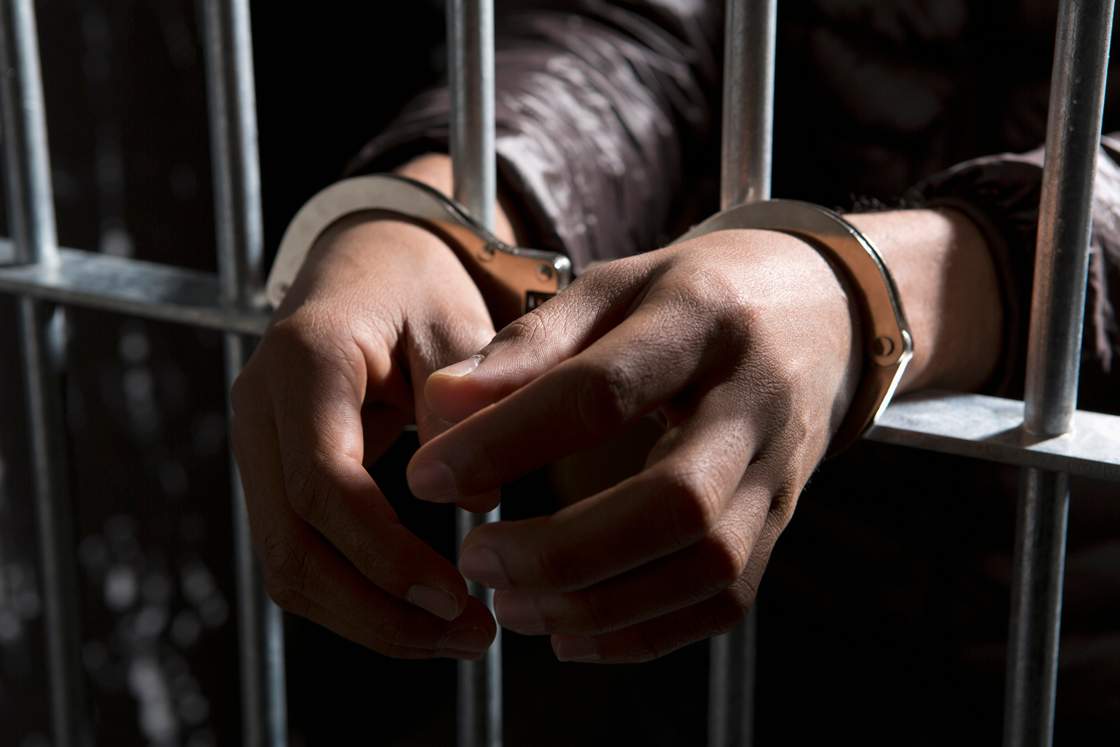 A prisoner behind bars with hands cuffed.
