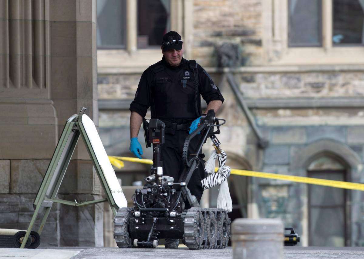 A police officer approaches a police bomb disposal robot holding a suspicious package on Parliament Hill in Ottawa on Thursday, March 28, 2013. 