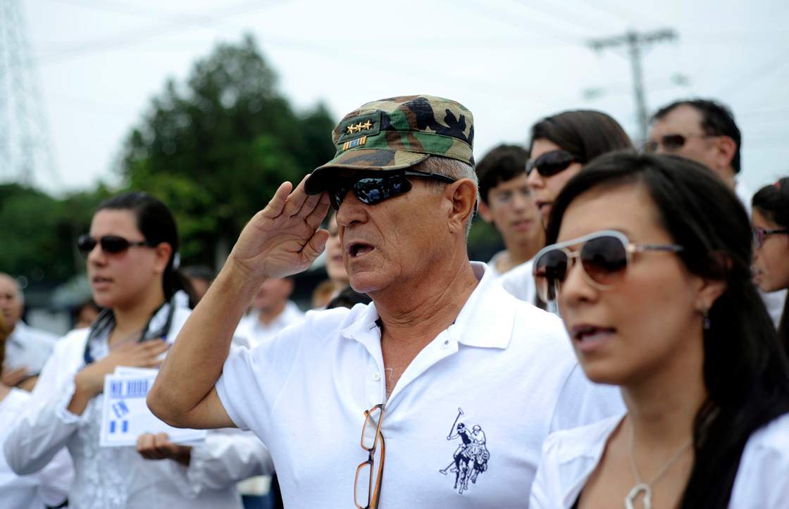 Supporters of former Guatemalan de facto President (1982-1983), retired General Jose Efrain Rios Montt, sing the national anthem during a protest against the latter's prosecution, outside a military prison at Matamoros in Guatemala City on May 12, 2013. Rios Montt was found guilty of genocide and war crimes on May 10 and sentenced to 80 years in prison in a landmark ruling stemming from massacres of indigenous people in his country's long civil war. Rios Montt thus became the first Latin American convicted of trying to exterminate an entire group of people in a brief but particularly gruesome stretch of a war that started in 1960, lasted 36 years and left around 200,000 people dead or missing.