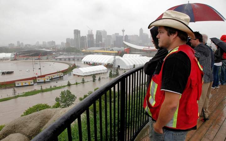 Calgarians look out over a flooded Calgary Stampede grounds and Saddledome due to the heavy rains in Calgary, Alta., Friday, June 21.THE CANADIAN PRESS/Jeff McIntosh.