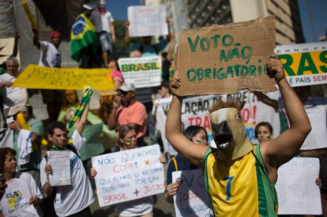 A masked demonstrator holds up a sign that reads in Portuguese "No mandatory vote," referring to Brazil's law that citizens are obligated to vote in all elections, during a protest march toward the Mineirao stadium where a Confederations Cup semifinal soccer match will be played between Brazil and Uruguay in Belo Horizonte, Brazil, Wednesday, June 26, 2013. The wave of protests that hit Brazil on June 17 began as opposition to transportation fare hikes, then expanded to a list of causes including anger at high taxes, poor services and high World Cup spending, before coalescing around the issue of rampant government corruption. (AP Photo/Felipe Dana)