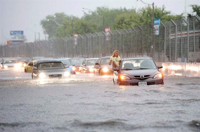 A woman gets gets out of her car to check it in flood water on Lakeshore West during a storm in Toronto on Monday, July 8, 2013.