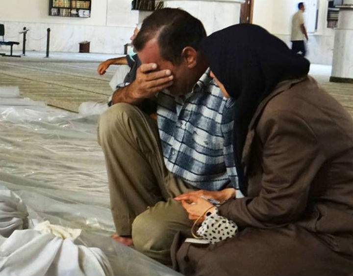 In this citizen journalism photo provided by the Local Committee of Arbeen, which has been authenticated based on its contents and other AP reporting, a man and woman mourn over the dead bodies of Syrian men after an alleged poisonous gas attack fired by regime forces, according to activists in Arbeen town, Damascus, Syria, .