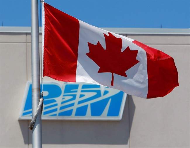The Canadian flag flies in front of the Research In Motion (RIM) company logo on one of their buildings in Waterloo, Ont., on June 29, 2012.