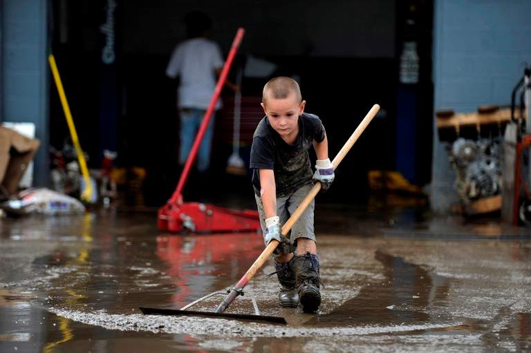 Michael Adamson, 5, uses a squeegee to clean the mud left by flood waters in front of T&M Automotive on Boston Ave in Longmont, Colorado on September 14, 2013. Clean up began on Saturday in downtown Longmont following heavy flooding in previous days. (Seth McConnell/The Denver Post via Getty Images)