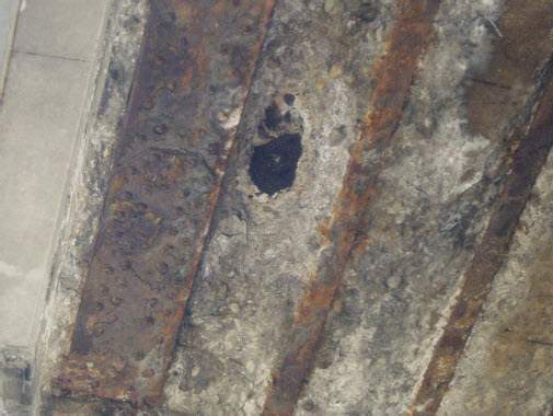 Photo of a hole in the bottom of the Dufferin Bridge from a Feb. 2008 report. The bottom of the asphalt surface is visible through a hole in the concrete.