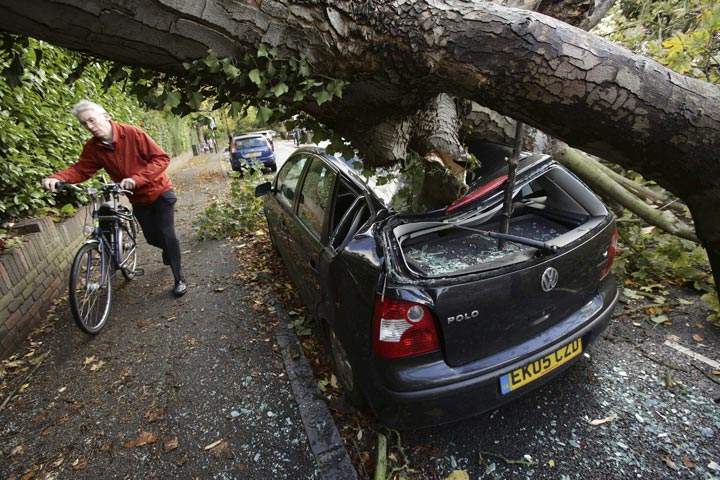 A car is crushed under a fallen tree as a man pushes a bicycle nearby following a storm, in Hornsey, north London, Monday Oct. 28, 2013. (Yui Mok /AP Photo/PA)