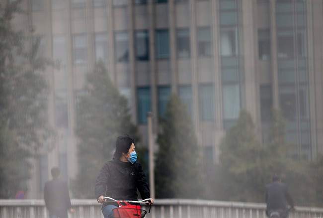 A woman wearing a face mask looks at the traffic as she bicycles on a road in Beijing Tuesday, Oct. 22, 2013. 