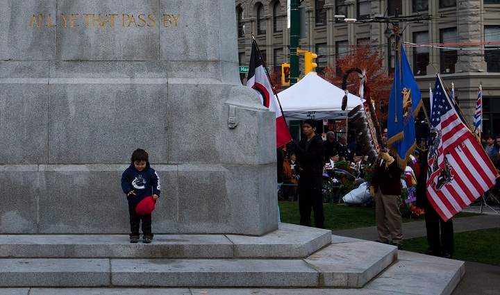 A young First Nations boy stands at the Victory Square Cenotaph as a colour party including veterans hold flags during a National Aboriginal Veterans Day ceremony in Vancouver, on Friday November 8, 2013. The ceremony is held to remember Aboriginal, Metis and Inuit men and women who served in the Canadian Forces. (The Canadian Press/Darryl Dyckber)