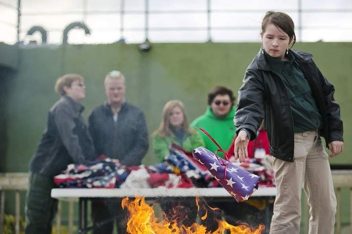 Lucas Payne, 15, left, and Marcus Bartlett, 15, members of Boy Scouts of America Troop 1053, stand next to Kaelyn Phillips, 15, and William Halstedt, 18, members of Venture Crew Group 9053, as Dorothy Gray, 14, member of Venture Crew Group 9053, throws a flag into the fire during a flag retirement ceremony Sunday, Nov. 10, 2013, in front of the USS LST 393 Veterans Museum in Muskegon, Mich. (AP Photo/The Muskegon Chronicle, Natalie Kolb)