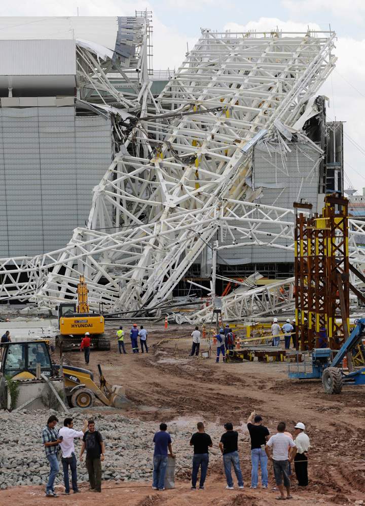 People stand in front of a metal structure that buckled on part of the Itaquerao Stadium in Sao Paulo, Brazil, Wednesday, Nov. 27, 2013 (Photo credit: AP Photo).