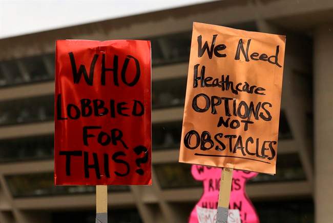 In this July 15, 2013 file photo, two signs that read "Who Lobbied For This?" and "We Need Healthcare Options, Not Obstacles" are held by attendees of a rally in front of Dallas city hall where a group of nearly 200 gathered to protest the approval of sweeping new restrictions on abortion in Texas. A U.S. appeals court on Thursday, Oct. 31, 2013, issued a ruling reinstating most of Texas' tough new abortion restrictions, which means as many as 12 clinics will not be able to perform the procedure starting as soon as Friday. 