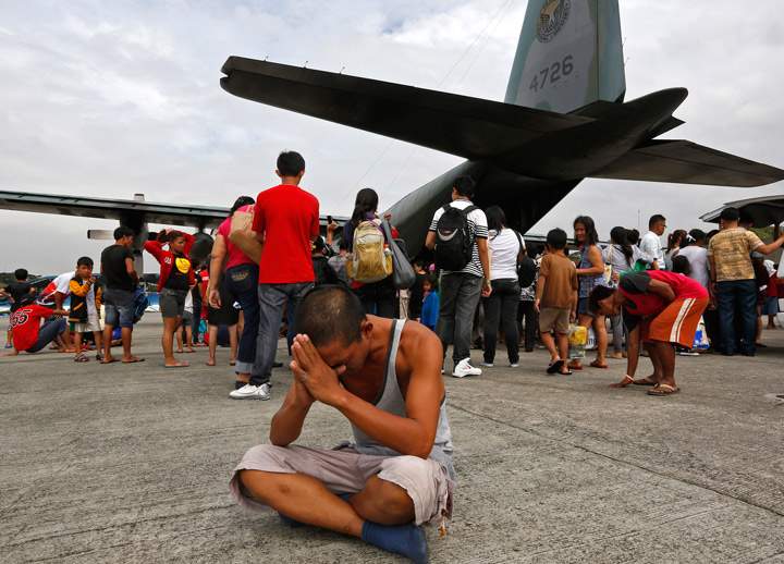 A survivor from Tacloban, which was devastated by Typhoon Haiyan gestures while sitting on the ground after disembarking a Philippine Air Force C-130 aircraft at the Villamor Airbase, Tuesday, Nov. 12, 2013, in Manila, Philippines. (Photo credit: AP Photo)