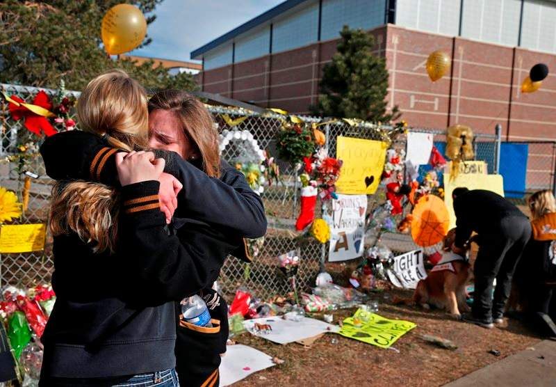 Arapahoe High School senior Lily Boettcher, right, and 2013 Arapahoe grad Joy Dafoe hug at a tribute site for severely wounded student Claire Davis, who was shot by a classmate during a school attack six days earlier at Arapahoe High School, in Centennial, Colo., Thursday Dec. 19, 2013. On Thursday, students were allowed back into school to retrieve their belongings. (AP Photo/Brennan Linsley).