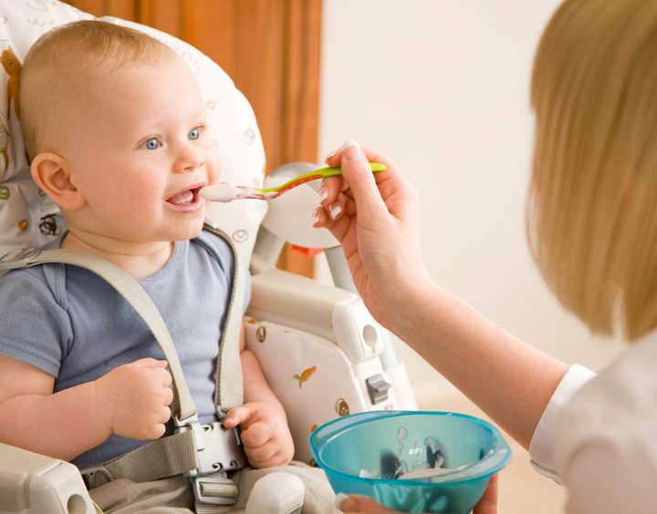Baby sitting in his highchair with his mother feeding him