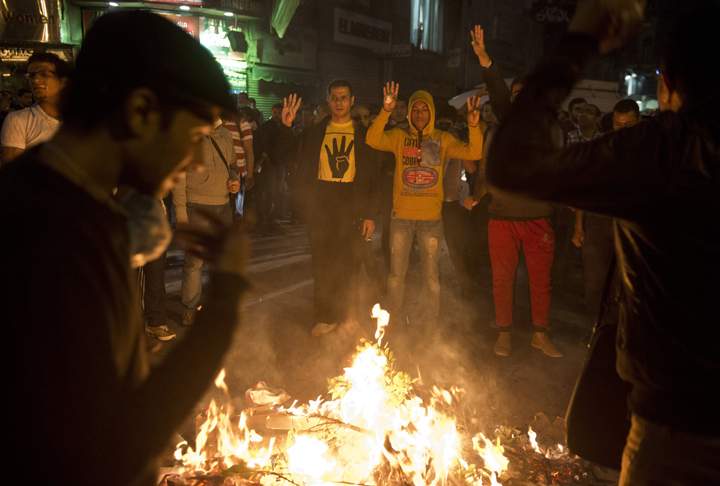 Egypt:Egyptian Muslim Brotherhood supporters flash the four-finger sign around a fire during a demonstration on Talaat Harb Square (near Tahrir square) on Dec. 1, 2013 in Cairo. Protesters were chanting in Tahrir Square “Down with the military regime!” “People want the fall of the regime!” and “Rabaa Rabaa,” as demonstrators flashed a four-finger sign that has become associated with a government crackdown on pro-Morsi supporters in Cairo’s Rabaa al-Adawiya square on Aug. 14. (Photo credit: Getty Images)