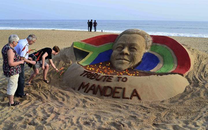 India:Tourists offer floral tributes near a sand sculpture of Nelson Mandela on a beach in Puri, India, Friday, Dec. 6, 2013. (Photo credit: AP Photo)