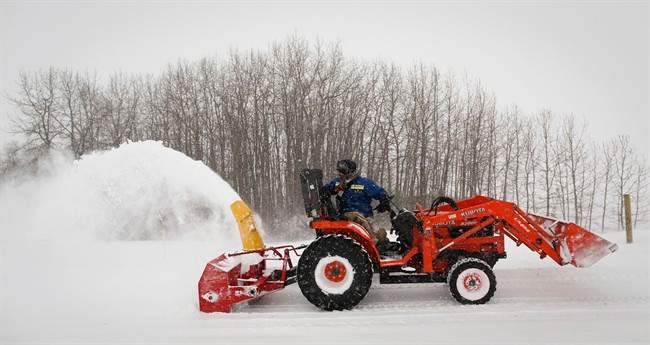 David Reid uses a snow blower mounted on a tractor to clear his driveway during a blizzard near Cremona, Alta., Monday, Dec. 2, 2013. 