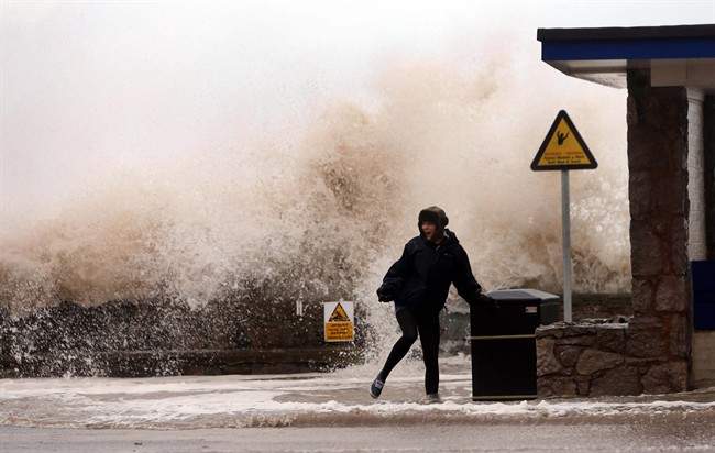 A woman stands in front of a huge wave on the seafront, in Rhyl, Wales, Thursday Dec. 5, 2013.