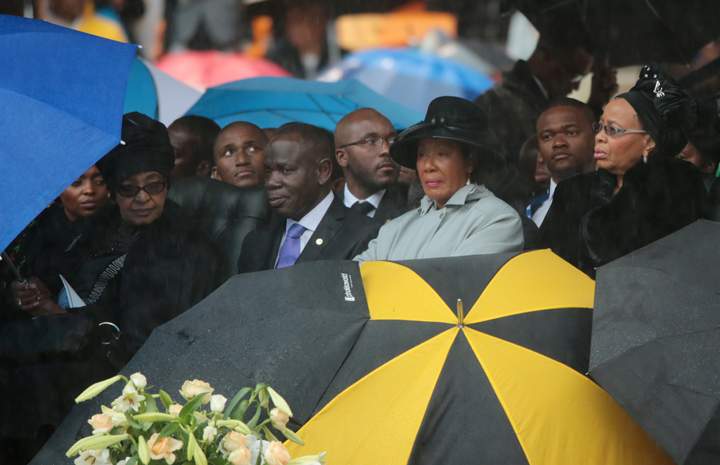 Winnie Madikizela-Mandela (L) sits under an umbrella as Graca Machel (R) looks on during the official memorial service for Mandela at the FNB Stadium on Dec.10, 2013 in Johannesburg, South Africa. (Photo credit: Getty Images)