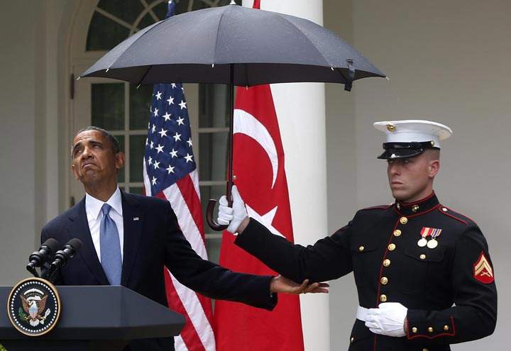 U.S. President Barack Obama looks to see if it is still raining as a Marine holds an umbrella for him during a news conference in the Rose Garden of the White House in Washington. (AP Photo/Charles Dharapak)