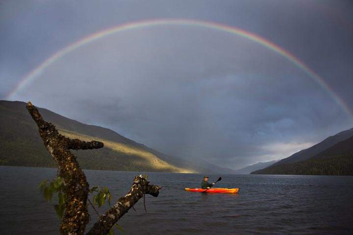 Darrell Trouton paddles a kayak as a rainbow stretches across the sky in Trout Lake, British Columbia. (The Canadian Press /Jason Franson)