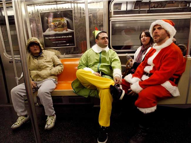 FILE - In this Dec. 11, 2010 file photo, John Paul, center, of Manhattan, dressed as an Elf and Michael Smallwood, of Brooklyn, dressed as Santa ride the E train downtown in New York for the annual SantaCon pub crawl where participants dress up in Santa and other Christmas themed outfits. 