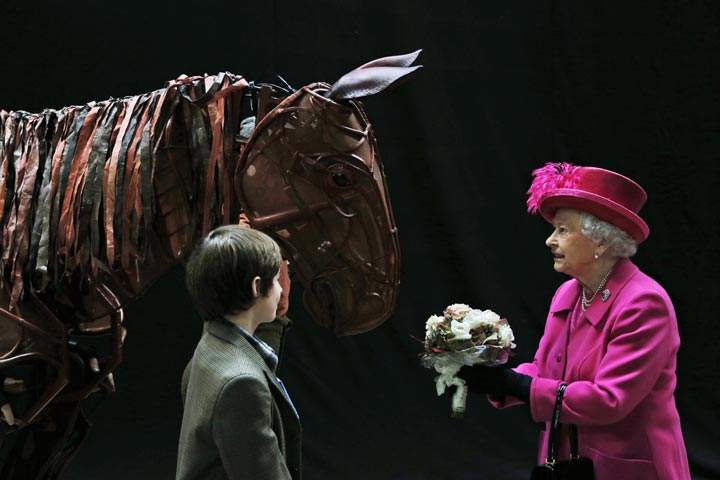 Queen Elizabeth II receives flowers from a child actor as she inspects the horse prop from the theatre production ‘War Horse’ during a visit at the National Theatre in London. (AP Photo/Lefteris Pitarakis)