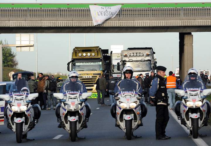 France:French policemen take position as trucks block a section of highway A25 in Englos to protest the “ecotax,” a controversial tax on heavy vehicles, on Dec. 2, 2013. French President Francois Hollande’s government has already been forced to suspend the planned introduction of a new environmental “ecotax” on commercial vehicles carrying cargo of more than 3.5 tonnes after violent protests in Brittany, a predominantly agricultural region in northwestern France. Opponents of the tax, which critics say unfairly penalises remote areas dependent on deliveries by road freight, are demanding it be scrapped altogether. (Photo credit: Getty Images)