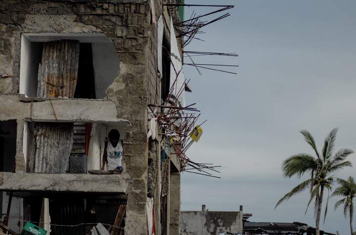 A typhoon survivor is seen through the missing wall of a damaged apartment building in Tacloban, Philippines, December 24, 2013. (Photo credit: AP Photo)