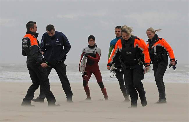Police officers accompany two surfers, centre, after they tried to enter the water during stormy weather, at the coastal town in Blankenberge, Belgium,Thursday, Dec. 5, 2013.