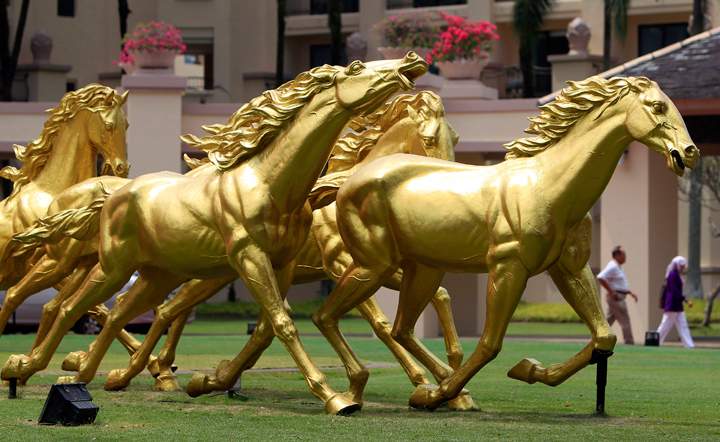 People walk past golden horse statues on display in front of a hotel in Kuala Lumpur, Malaysia, Saturday, Jan. 25, 2014. (Photo credit: Lai Seng Sin/AP Photo)