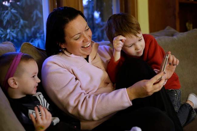 Julie Young, a Boston-based behavioral analyst, center, sits with her sons Nolan, 3, left, and Jameson, 4, right, while looking at a smart phone at their home, in Boston, Monday, Jan. 27, 2014.