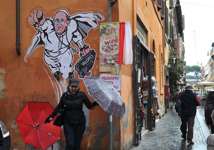 A woman poses in front of a street art mural showing Pope Francis as a superman, flying through the air with his white papal cloak billowing out behind him and holding a bag bearing the word ‘Values’, by Italian street artist Maupal in downtown Rome near the Vatican on January 29, 2014.