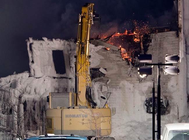 A crane knocks down a wall after a fatal fire destroyed a seniors residence in L'Isle-Verte, Que., Thursday, January 23, 2014.