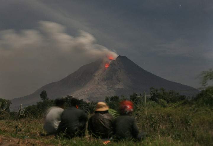 In this Monday, Jan. 13, 2014 photo, Indonesian men watch as Mount Sinabung erupts with molten rocks and hot gasses in Jeraya, North Sumatra, Indonesia.