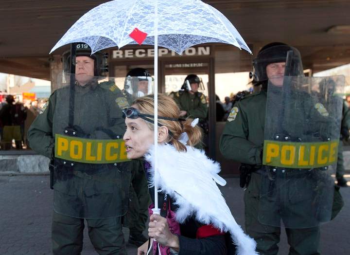 A female demonstrator dressed as an angel kneels in front of a line of police officers in riot gear in front of a hotel Saturday, May 5, 2012.