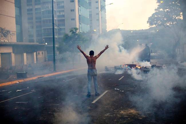 A demonstrator raises his arms toward the Bolivarian National Police (BNP) firing tear gas and a water canon in the Altamira neighborhood of Caracas, Venezuela, Wednesday, Feb. 19, 2014.