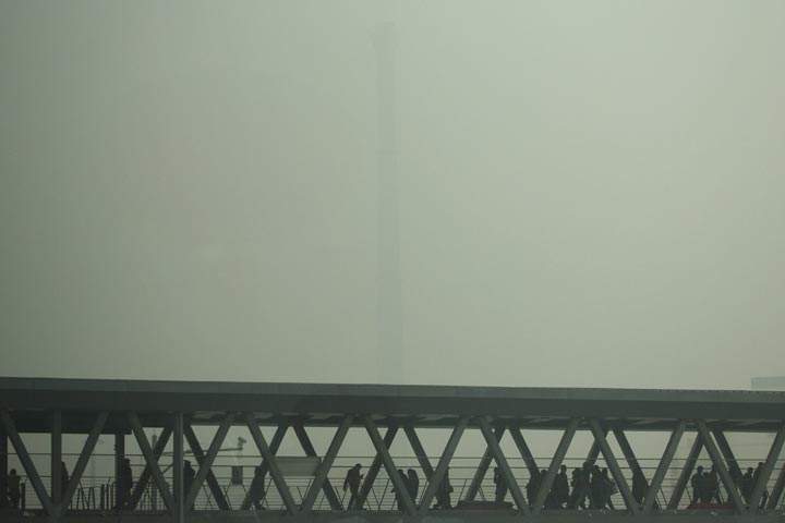 A chimney of a heating plant is obscured by heavy haze as commuters walk through a bridge on a severely polluted day in Beijing Tuesday, Feb. 25, 2014. (AP Photo/Alexander F. Yuan)