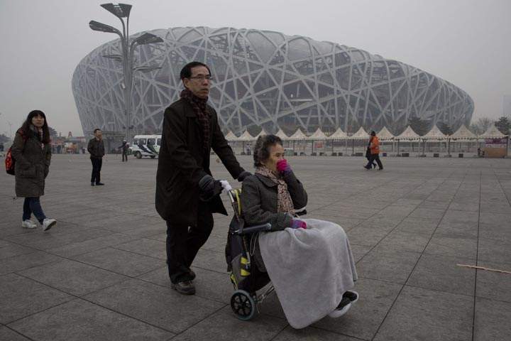 A woman in a wheelchair covers her face as she passes by the iconic bird’s nest National Stadium on a hazy day in Beijing, China, Sunday, Feb. 23, 2014. (AP Photo/Ng Han Guan)